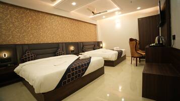 A hotel room with two beds, a desk, a chair, a TV, and a ceiling fan.