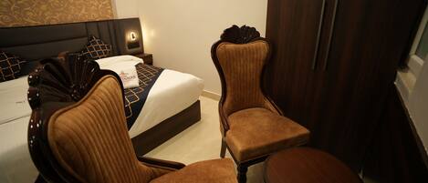 A hotel room with a bed, two upholstered chairs, a wooden side table, and a wardrobe.