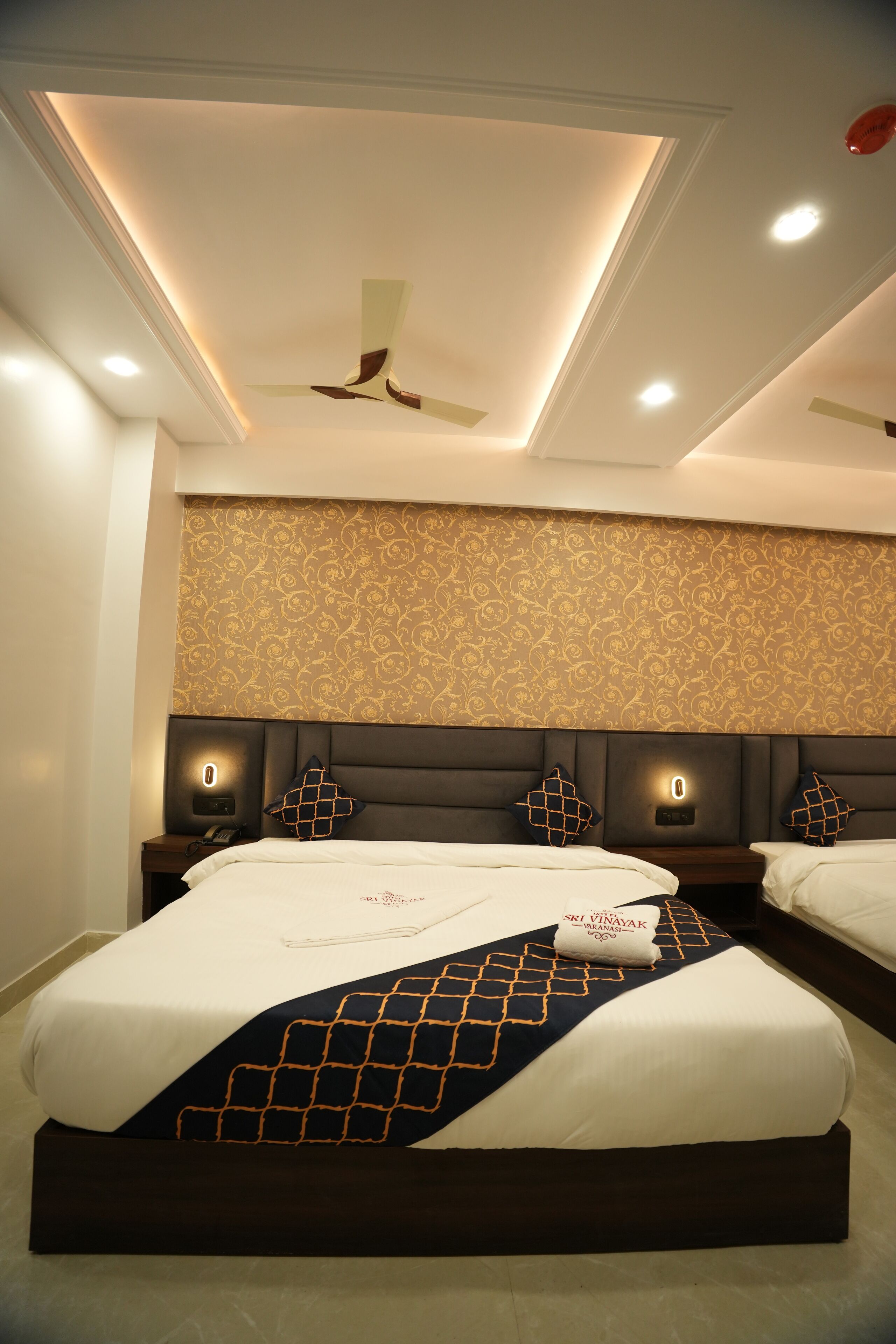 A modern hotel room with a large bed, a ceiling fan, and a patterned wallpaper.