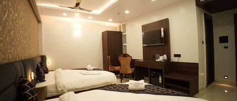 A hotel room with two beds, a desk, a chair, a TV, and a minibar.