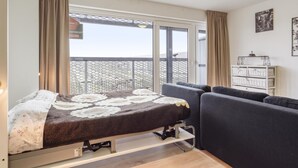 Une chambre à coucher comprenant un lit, un canapé, une table de chevet, une fenêtre avec des rideaux et une vue sur un balcon.
