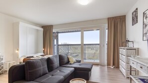 Un salon moderne avec un canapé d’angle, une petite table ronde et un balcon offrant une vue agréable.