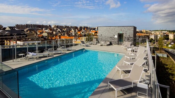 Une piscine sur le toit, dotée de chaises longues et bordée d’un mur en pierre.
