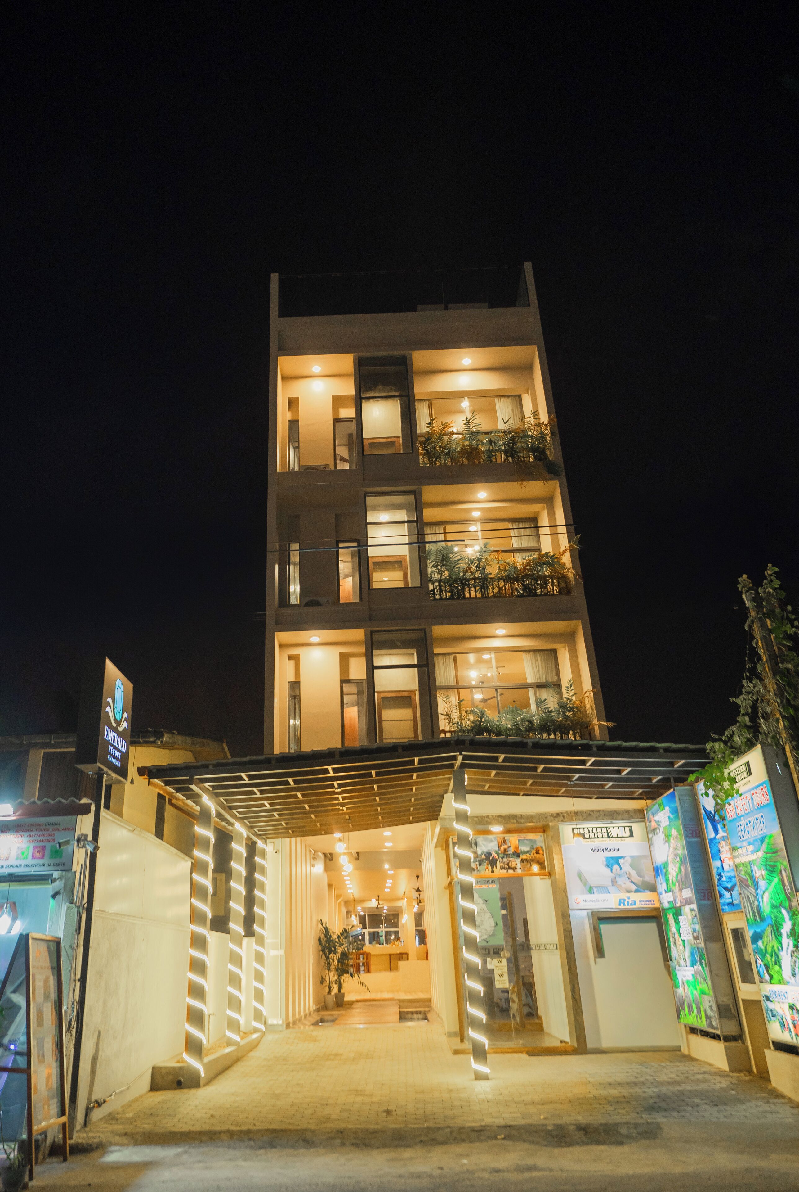 Un hôtel à plusieurs étages, doté de balcons illuminés et d’un espace d’entrée abrité.