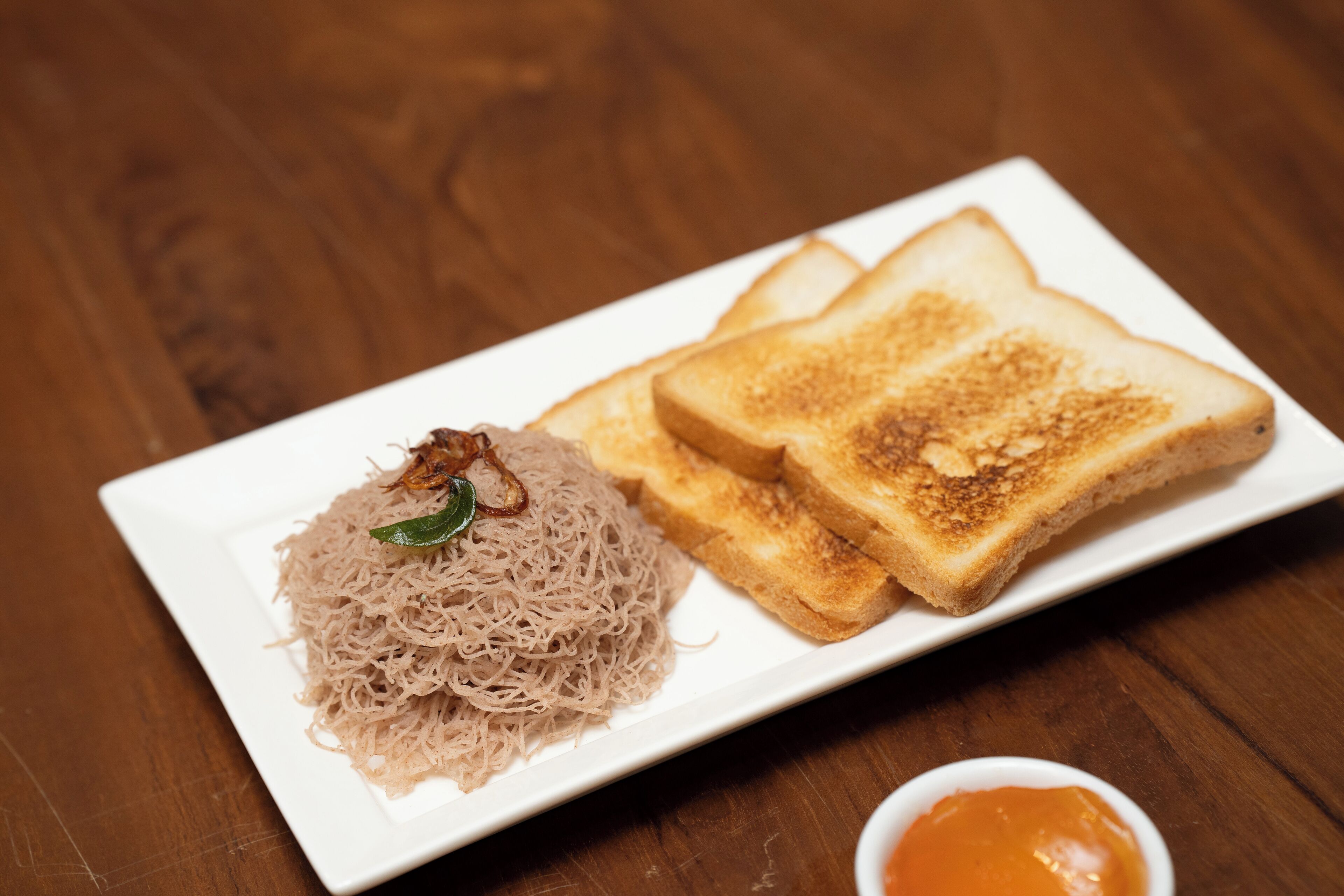 A plate with noodles and toasted bread on a wooden table.