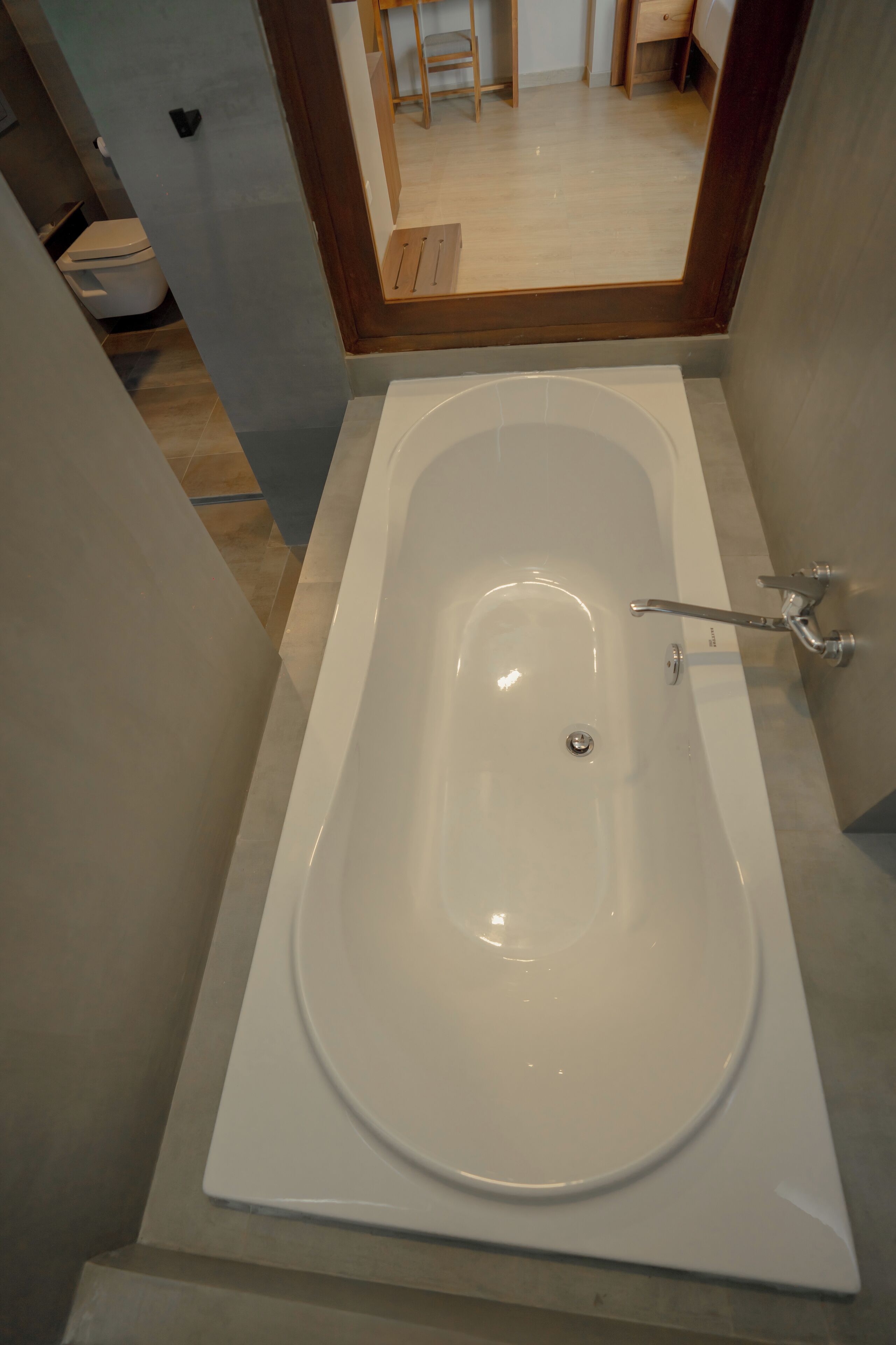 A modern bathroom with a freestanding bathtub, a visible toilet, and a wooden floor.