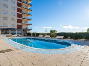 A swimming pool with lounge chairs, a supermarket, and a building with balconies. - Apartment with excellent beachfront location (Santa Susanna)