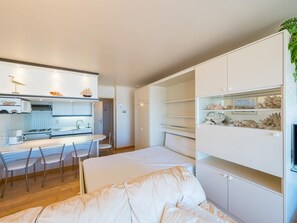 A modern kitchen with white cabinets, a dining area with a white table and chairs, and a built-in shelving unit with decorative items. - Studio with sea view and parking space (Middelkerke)