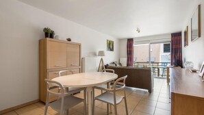 A modern kitchen with a dining area, featuring a round table with chairs, a cabinet, and a radiator. - Cosy flat close to the beach (Koksijde)