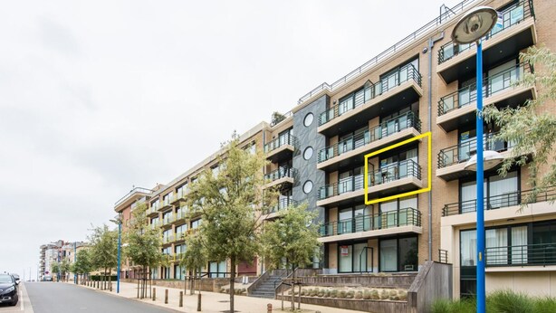 A modern multi-story building with balconies, a pedestrian walkway, and a street with parked cars. - Cosy flat close to the beach (Koksijde)