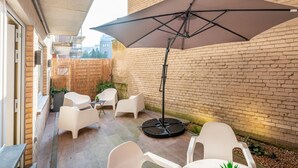 Un patio con sillas de plástico blancas, una mesa redonda y un paraguas grande.