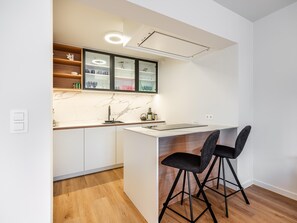 Eine moderne Küche mit weißen Schränken, einer Marmor-Spritzschutzwand und einer integrierten Kücheninsel mit Barhocker.