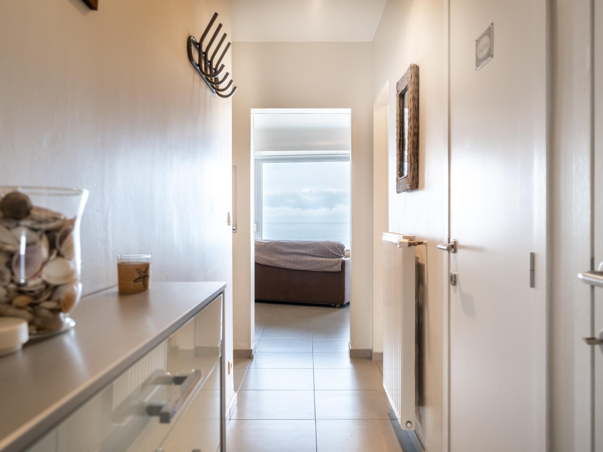 A hallway leading to a bedroom with a view of the sea, a radiator, and a coat rack.