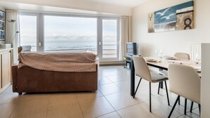 Una camera d'albergo moderna con una grande finestra vista mare, un letto accogliente, un angolo ristoro e un televisore a schermo piatto.