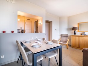A modern dining area with a table set for four, a sofa, a cabinet, and a mirror. - Beautiful flat with frontal sea views (Koksijde)