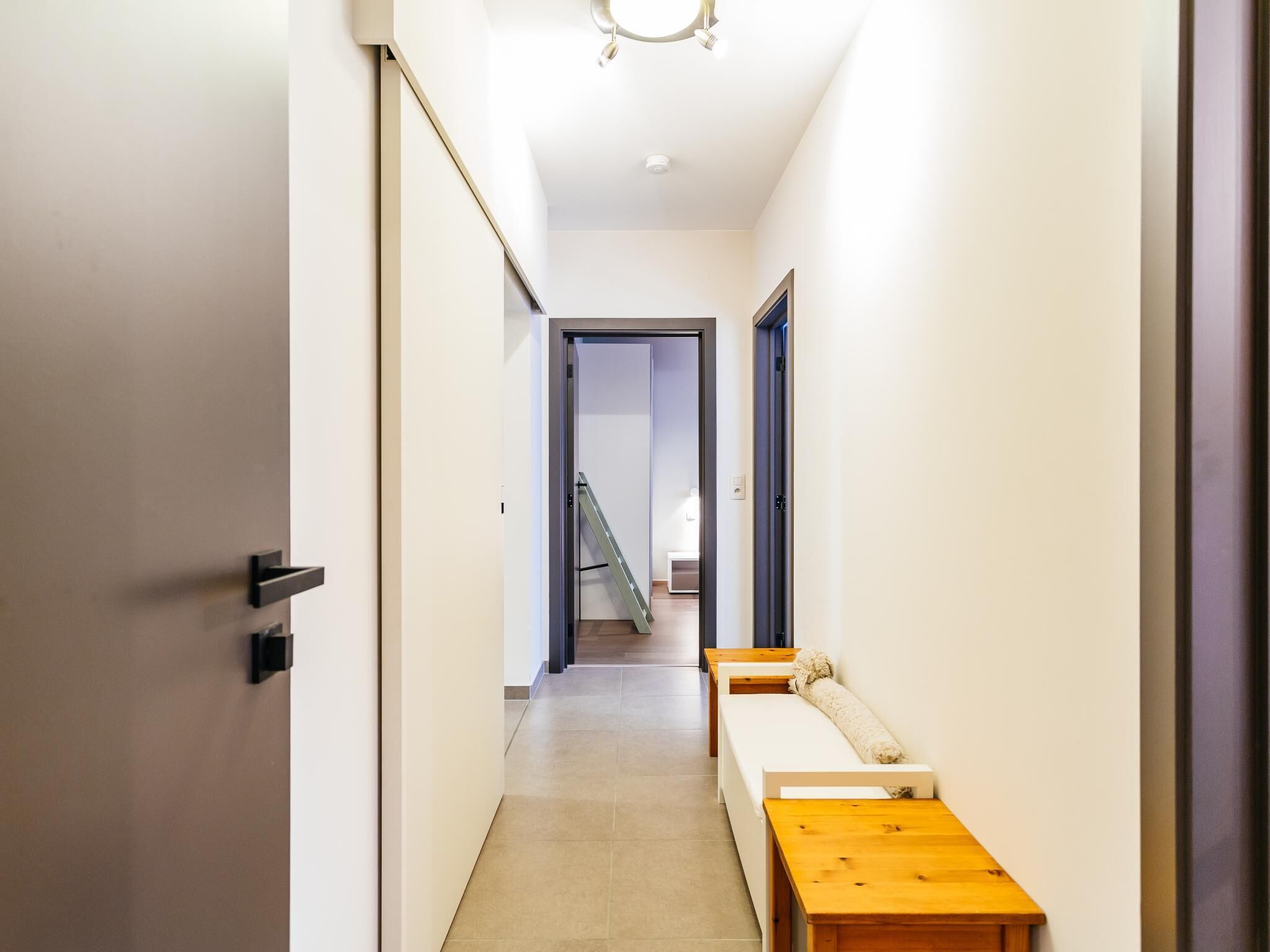 A narrow hallway with a wooden bench and a door on the left.