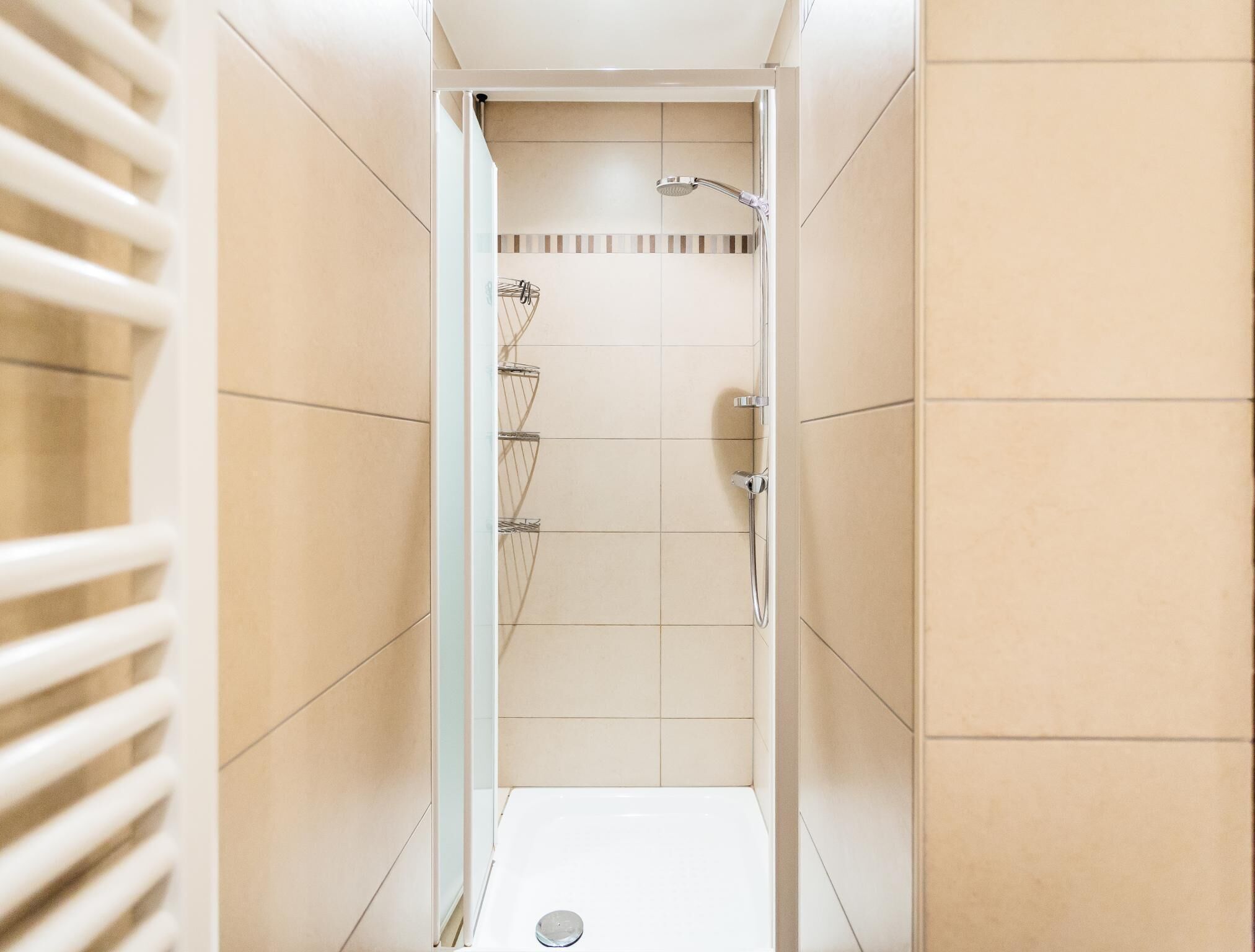 A narrow, tiled shower stall with a handheld showerhead and a wall-mounted faucet.
