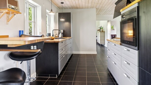 Eine moderne Küche mit Holzarbeitsplatte, schwarzen Barhocker, integriertem Backofen und einem großen Fenster.