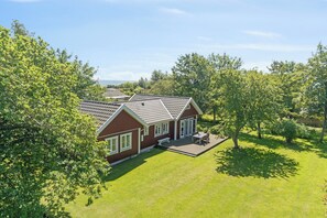 Ein zweistöckiges Haus mit Terrasse, umgeben von Bäumen und einem gepflegten Rasen.