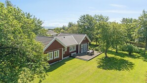 Ein zweistöckiges Haus mit Terrasse, umgeben von Bäumen und einem gepflegten Rasen.