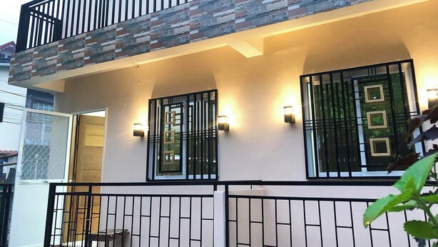 Uma casa de dois andares com sacada, portão fechado e pequeno alpendre.