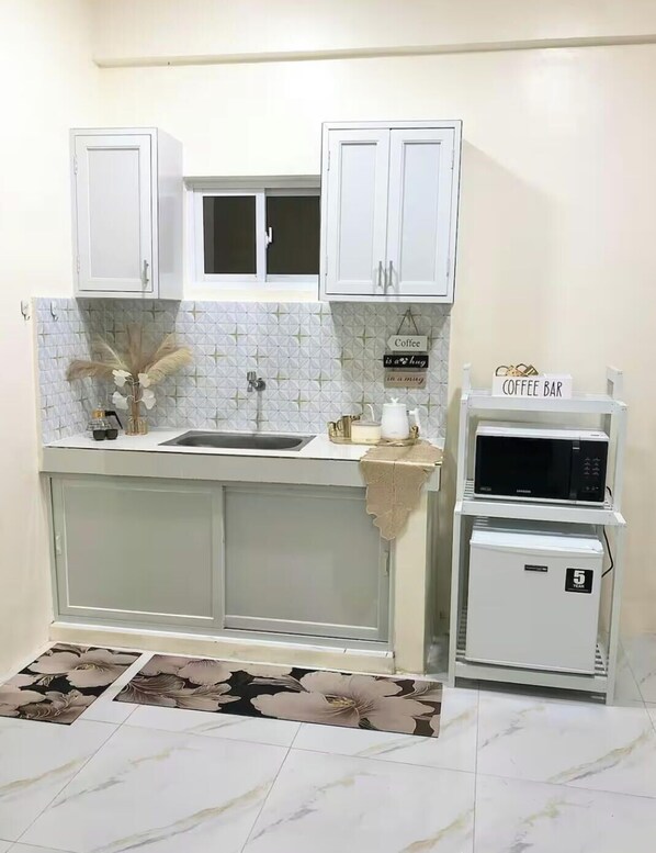 Una cocina con armarios blancos, un fregadero, un microondas y una zona para café.