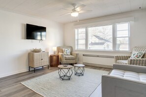 Ein Wohnzimmer mit Flachbildfernseher, zwei runden Tischen, einer Couch und einem Deckenventilator.