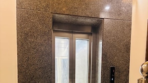 An elevator with a metallic finish, a control panel, and a marble floor. - Hotel Santosh Heritage (Pushkar)