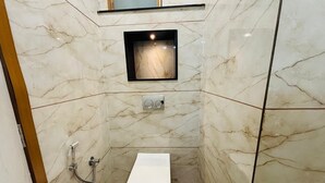 A small, modern bathroom with a white toilet, a shower, and a marble wall. - Hotel Santosh Heritage (Pushkar)