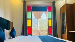 A bed with a white and blue quilt, a wooden headboard, and a view of a balcony with colorful window frames. - Hotel Santosh Heritage (Pushkar)