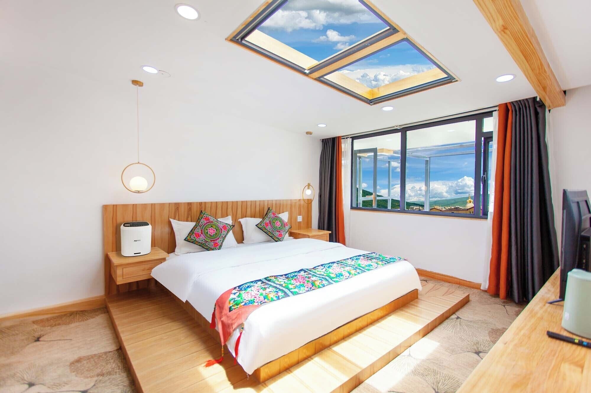 A modern hotel room with a skylight, a large bed, a wooden headboard, a bedside table with a lamp, and a view of the landscape.