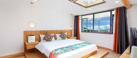 A modern hotel room with a skylight, a large bed, a wooden headboard, a bedside table with a lamp, and a view of the landscape.
