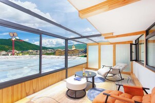 Una camera moderna con ampie finestre, vista su un paesaggio montuoso e un angolo relax con tavolo e sedie.