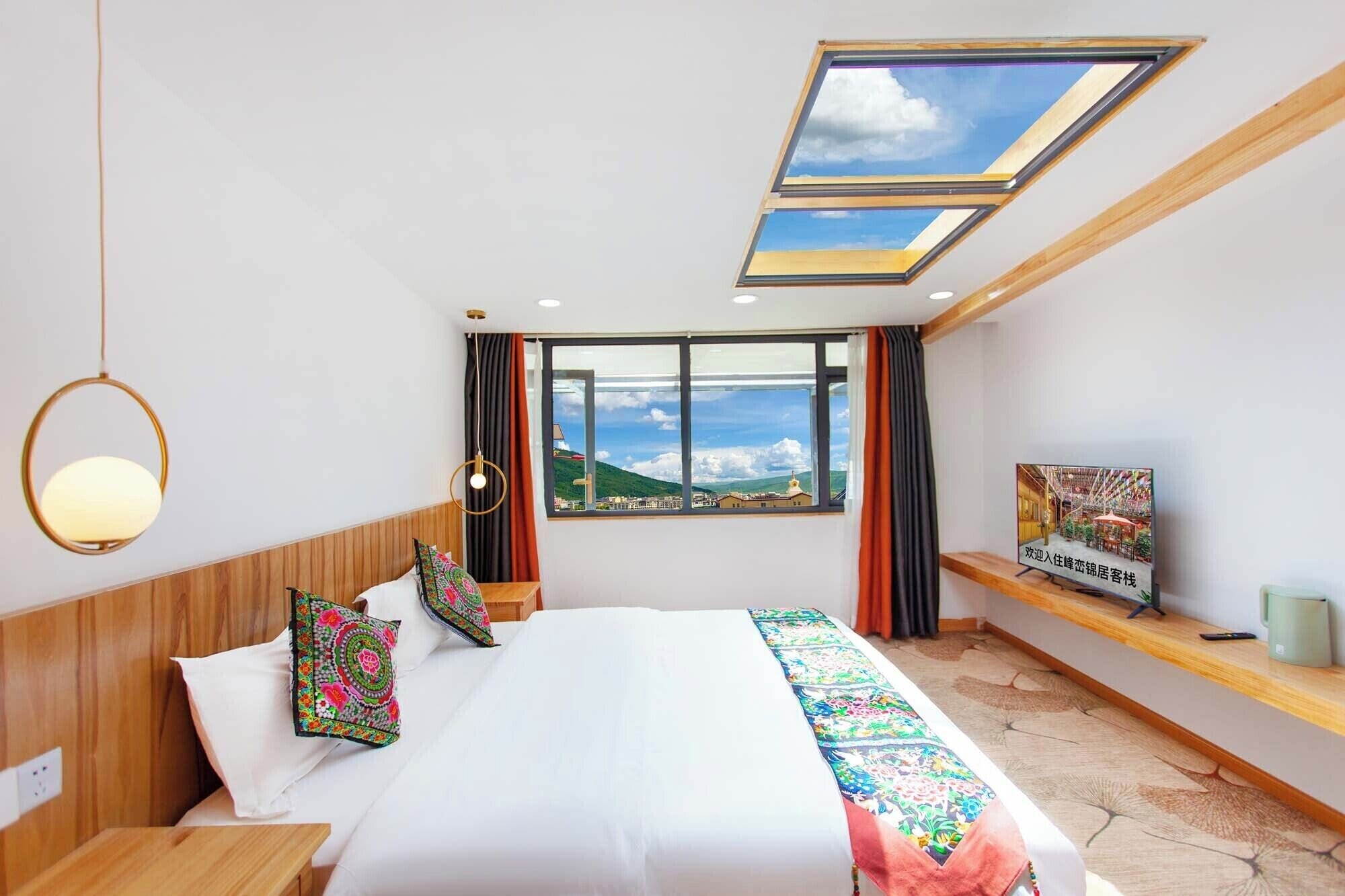 Quarto de hotel com uma cama grande, uma claraboia, vista para as montanhas e uma estante com um aviso.