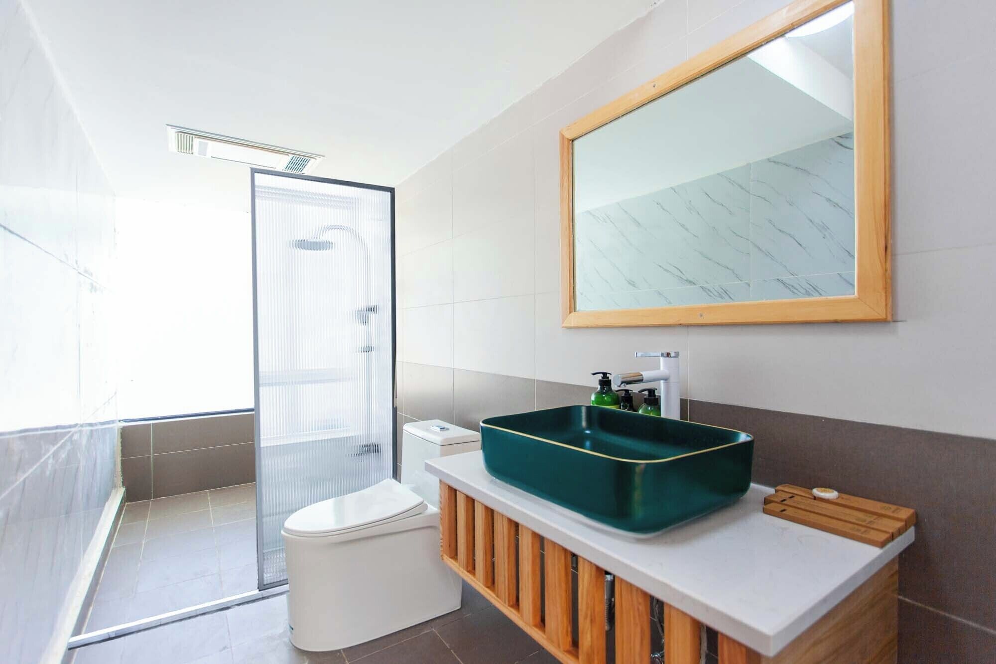Un baño moderno con un espejo grande, un lavabo verde y una cabina de ducha.