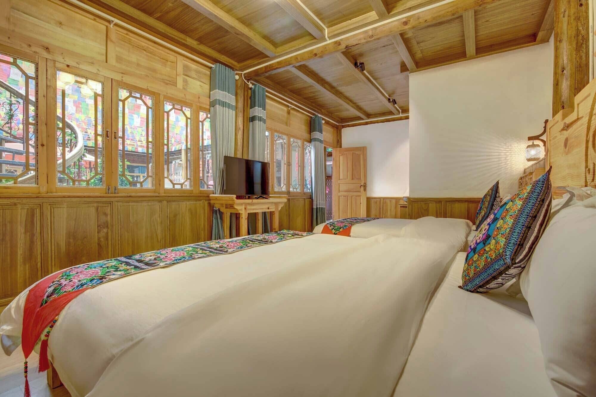 A wooden room with a bed, a television on a small table, and large windows with stained glass.