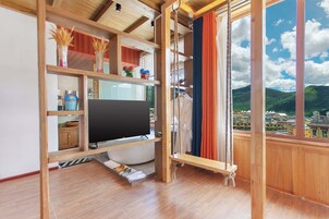 Una stanza con una grande televisione a schermo piatto, mensole di legno, un accappatoio appeso e vista sulla città attraverso un'ampia finestra.