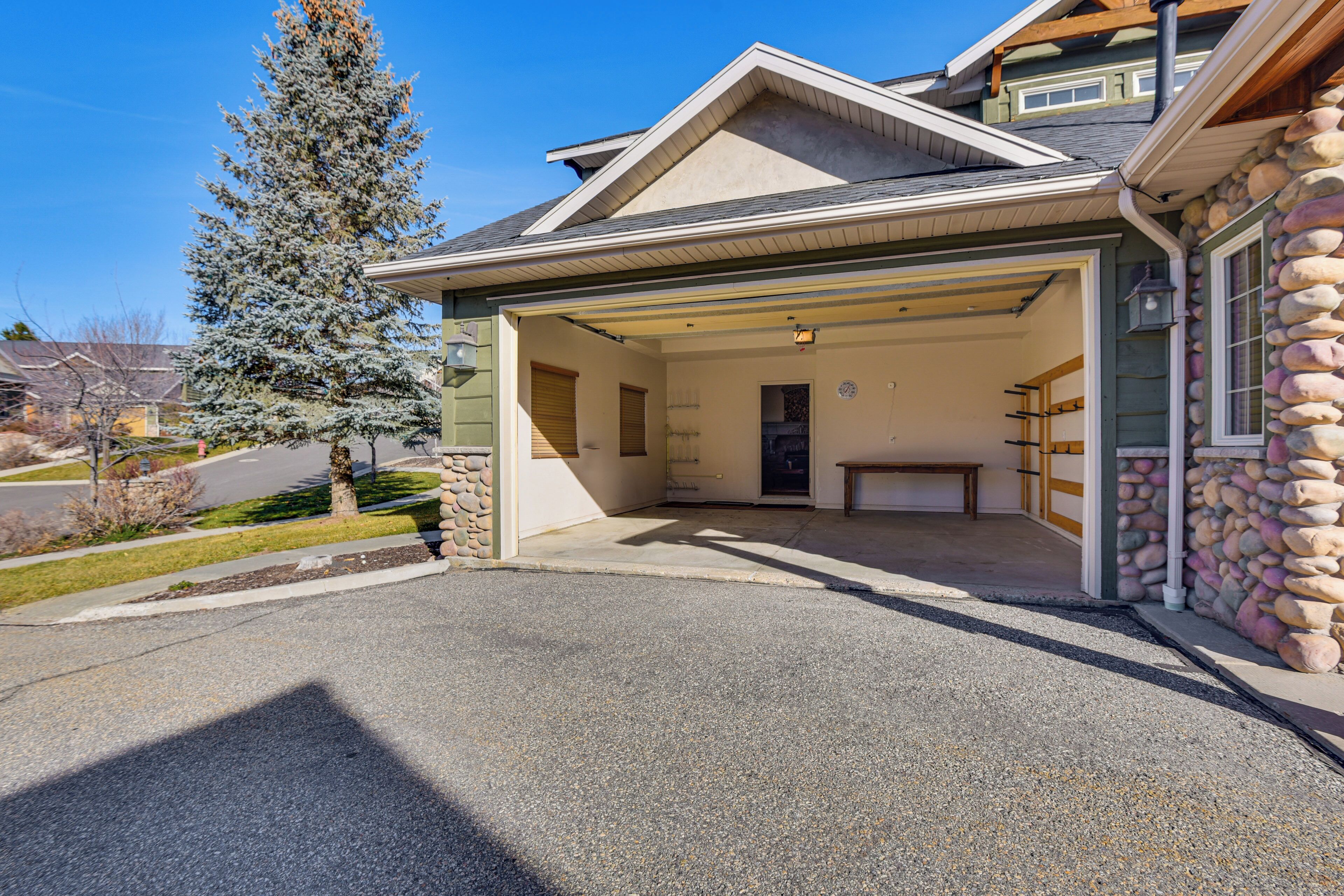 A two-story house with a garage, stone exterior, and a large evergreen tree in front.