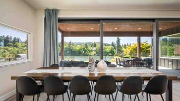 Un espace repas avec une grande table, des chaises noires et une vue sur un lac et une forêt.