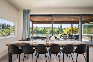 Un espace repas avec une grande table, des chaises noires et une vue sur un lac et une forêt.