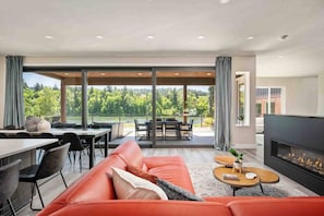 Un salon moderne comprenant un canapé, une table à manger, des chaises, une cheminée et une grande fenêtre donnant sur un paysage arboré.