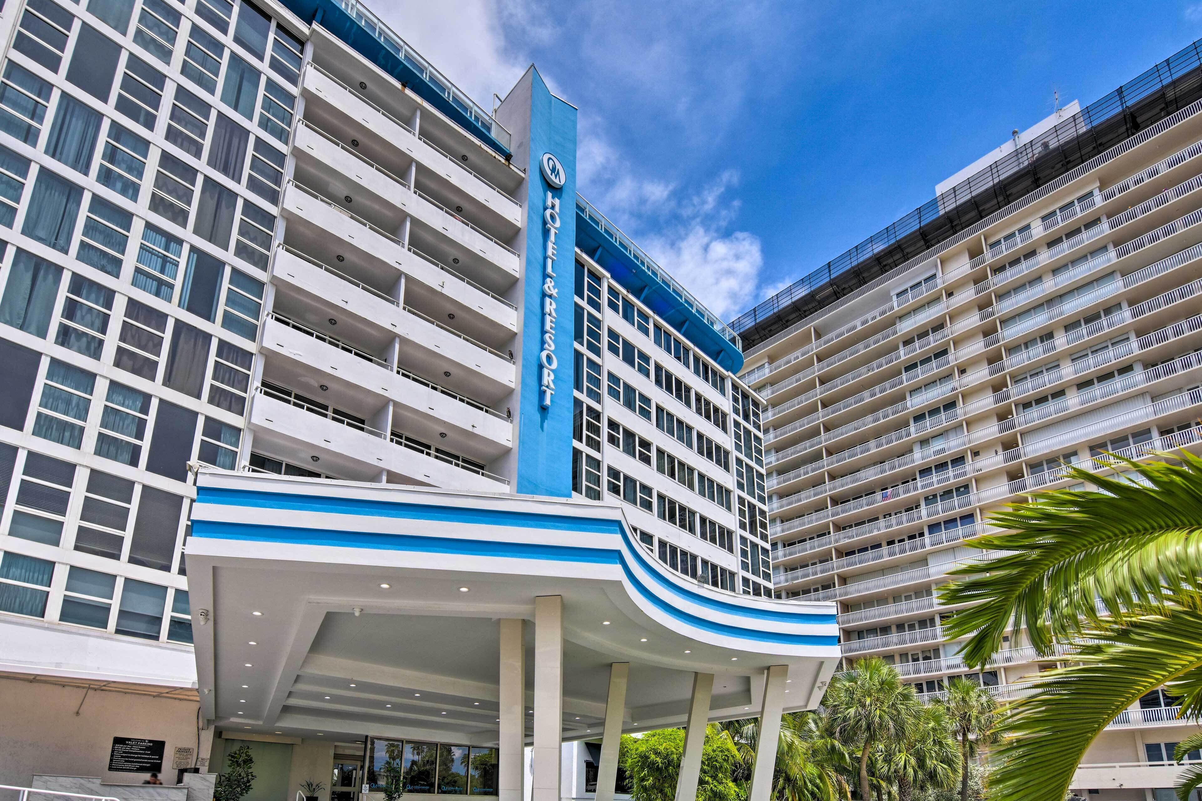 Un hotel de varios pisos con una fachada destacada en azul y blanco, que presenta balcones y una zona de entrada cubierta.