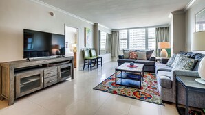 A modern living room with a flat-screen TV, a sofa, a coffee table, and a TV stand. - Steps to Sand! 10th-Floor Ocean Manor Unit w/ Pool (Fort Lauderdale)