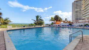 A swimming pool with lounge chairs and palm trees, surrounded by a tall building. - Steps to Sand! 10th-Floor Ocean Manor Unit w/ Pool (Fort Lauderdale)