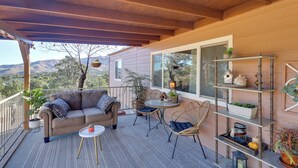 A covered patio with a sofa, chairs, and a small table, overlooking a scenic view. - Hualapai Mtn Views on 2 Acres: 'Thunderhead' Home (Kingman)