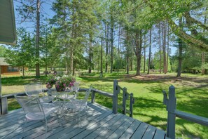 A wooden deck with outdoor furniture, surrounded by a grassy area and tall trees. - Sturgeon River Retreat: Fish, Raft & Relax (Indian River)