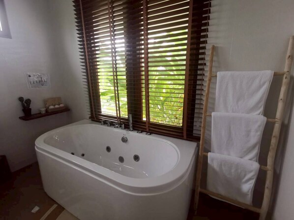 A bathroom with a freestanding bathtub, wooden blinds, a towel rack, and a small shelf with toiletries.