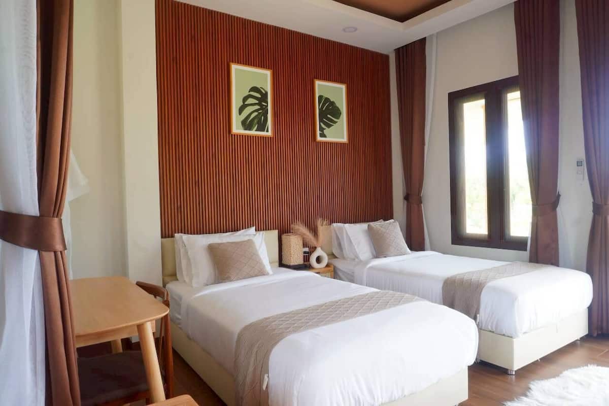 A hotel room with two beds, a wooden headboard, a small table, and a window with curtains.