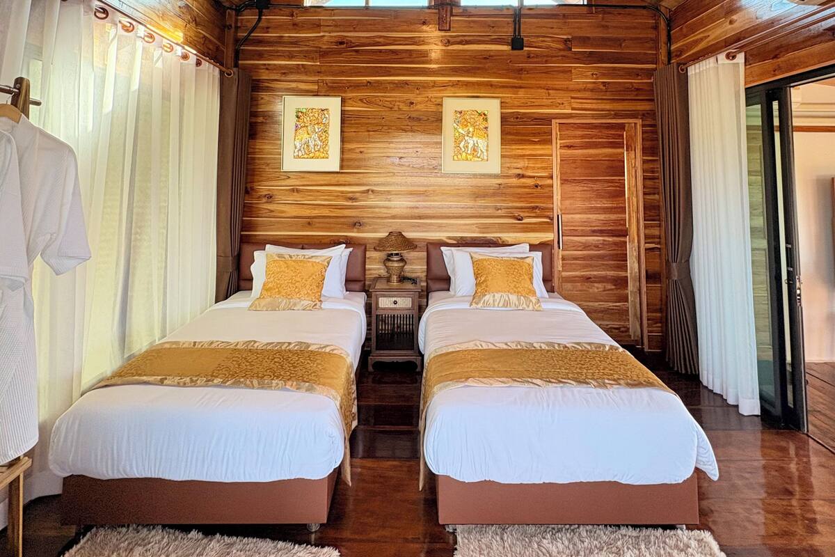A wooden cabin-style room with two beds, a ceiling fan, and a large window.