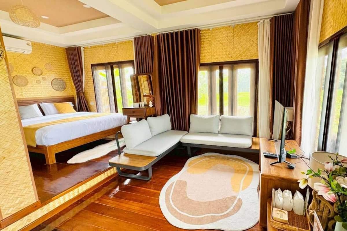 A hotel room with a bed, sofa, desk, and large windows.